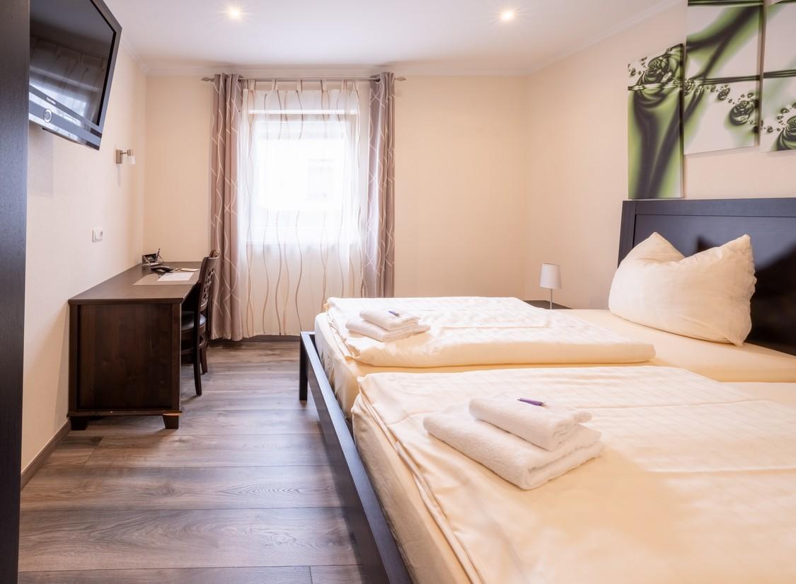 Gemütliches Hotelzimmer mit Doppelbett, dunklem Holzmobiliar und hellem Ambiente.