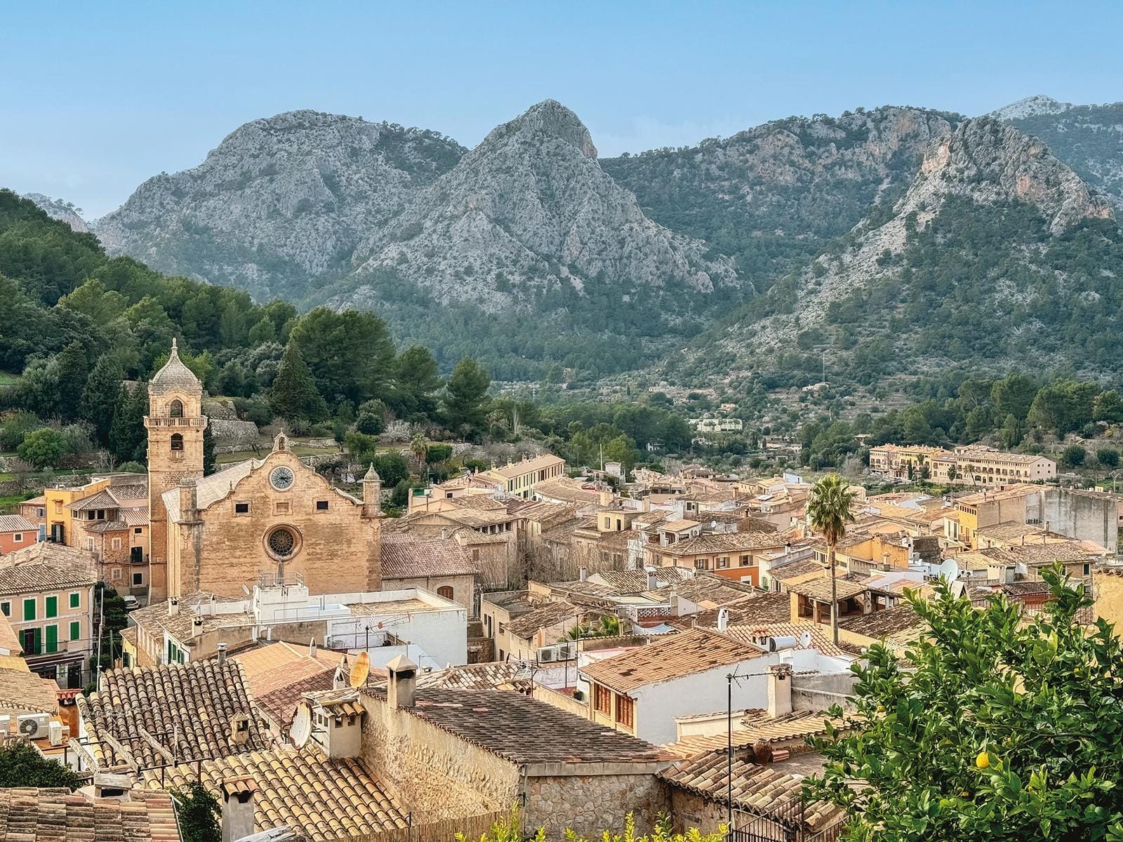 Spanien, Dorf in den Bergen mit Kirche vor bewaldeten Felsen und blauen Himmel.