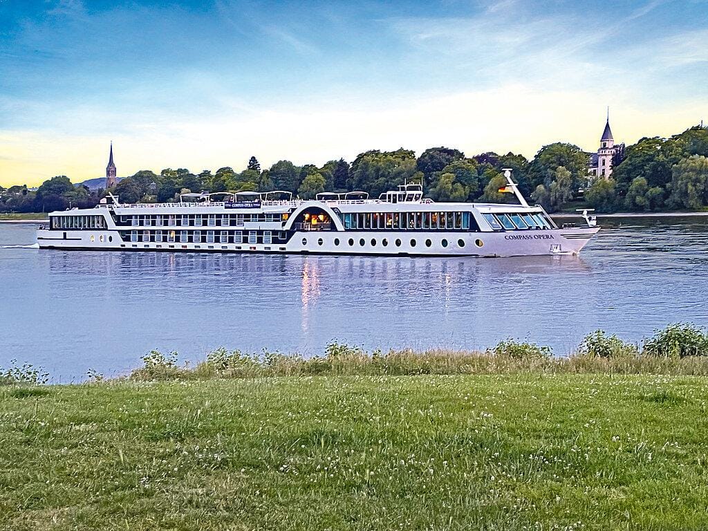 Ein Flusskreuzfahrtschiff auf dem Rhein in Deutschland, gesäumt von grüner Natur und Kirchtürmen.
