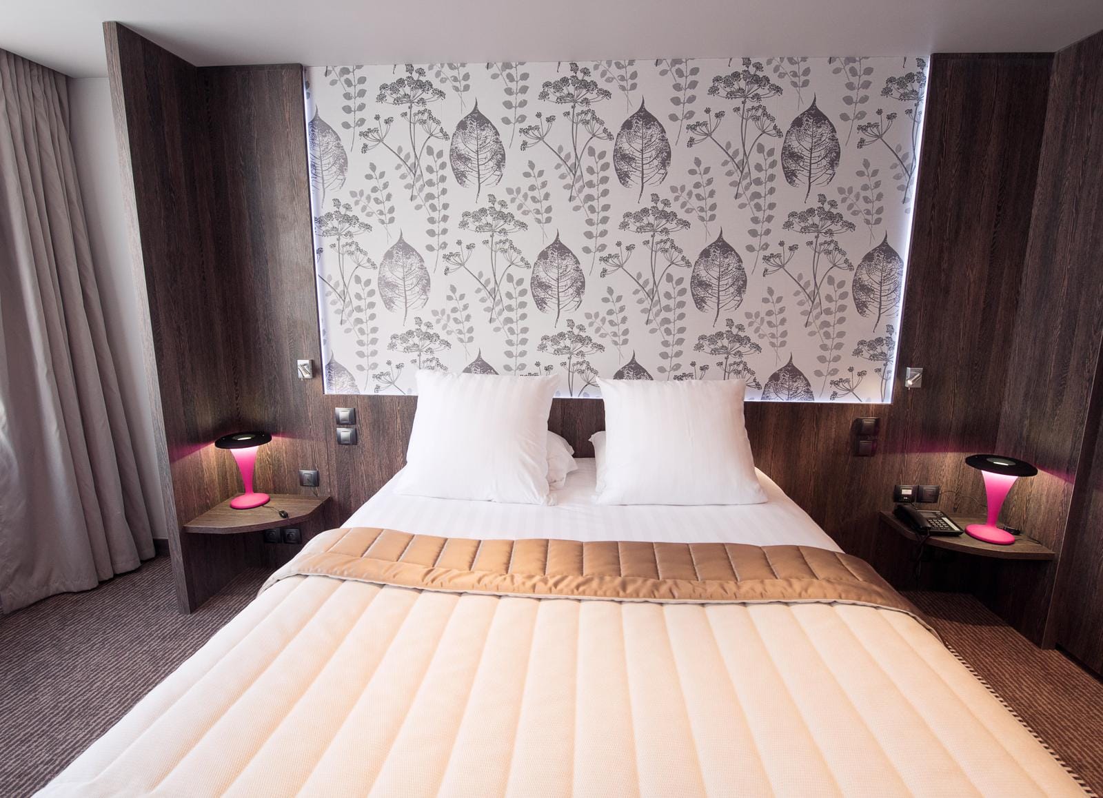 Modernes Hotelzimmer mit floralem Tapetenmuster, weißen Kissen und rosa Lampen.