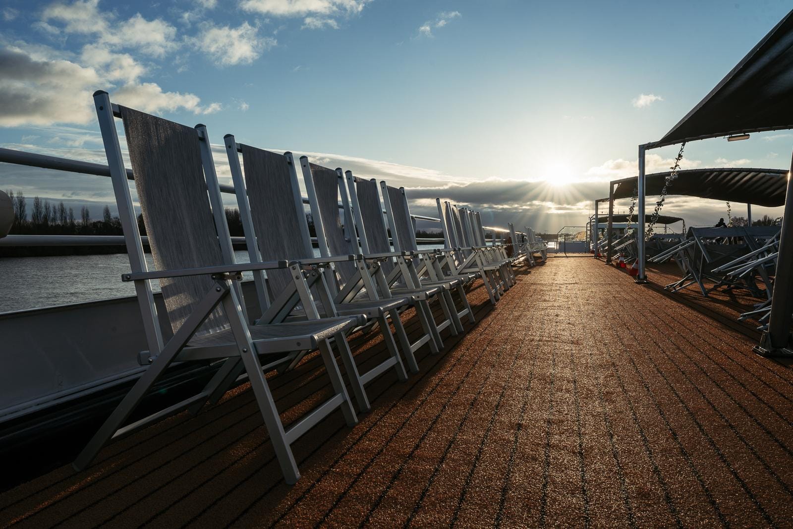 Sonnendeck eines Kreuzfahrtschiffs bei Sonnenuntergang mit Liegestühlen und Flussblick.