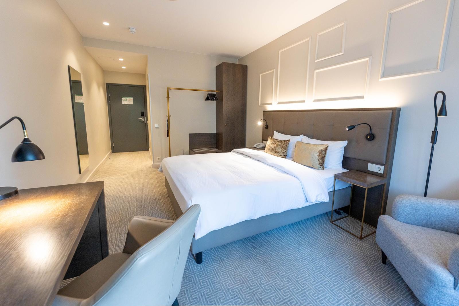 Modernes Hotelzimmer mit Doppelbett, Schreibtisch, grauem Teppich und stilvoller Beleuchtung.