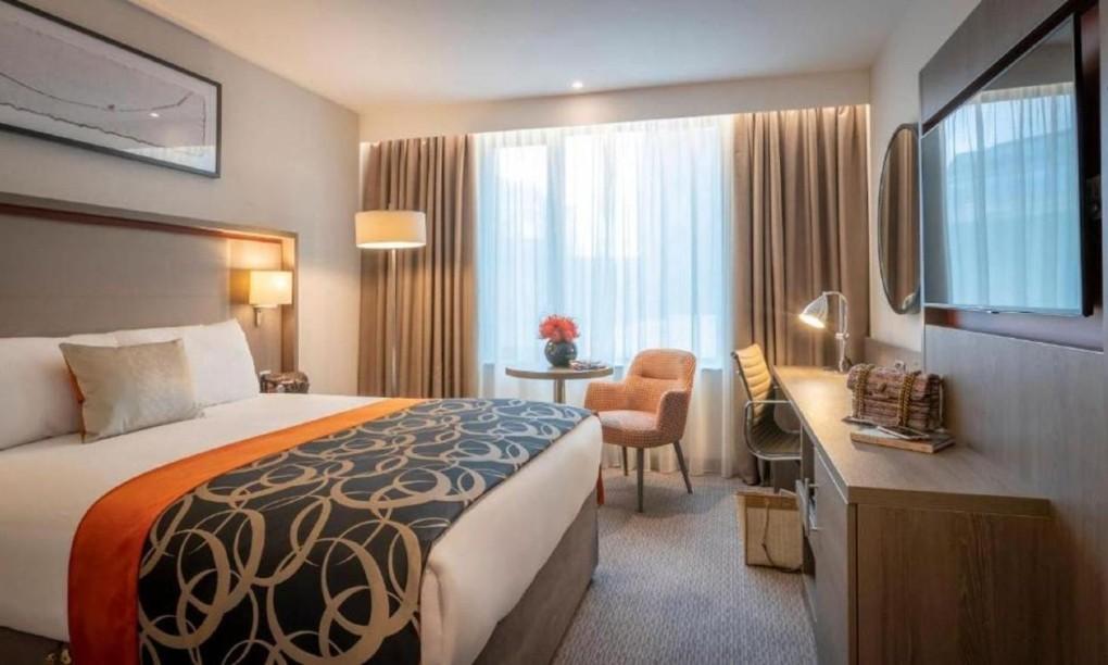 Modernes Hotelzimmer mit Kingsize-Bett, orangem Akzent, Schreibtisch, Sessel, stilvolles Ambiente.