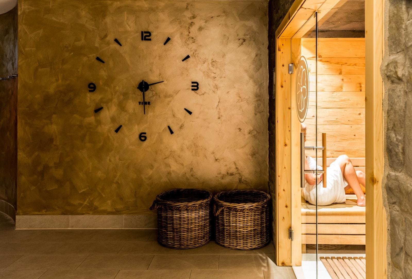 Elegante Sauna mit Holzwänden, Uhr an goldener Wand, zwei Rattan-Körbe im Hotel-Spa.