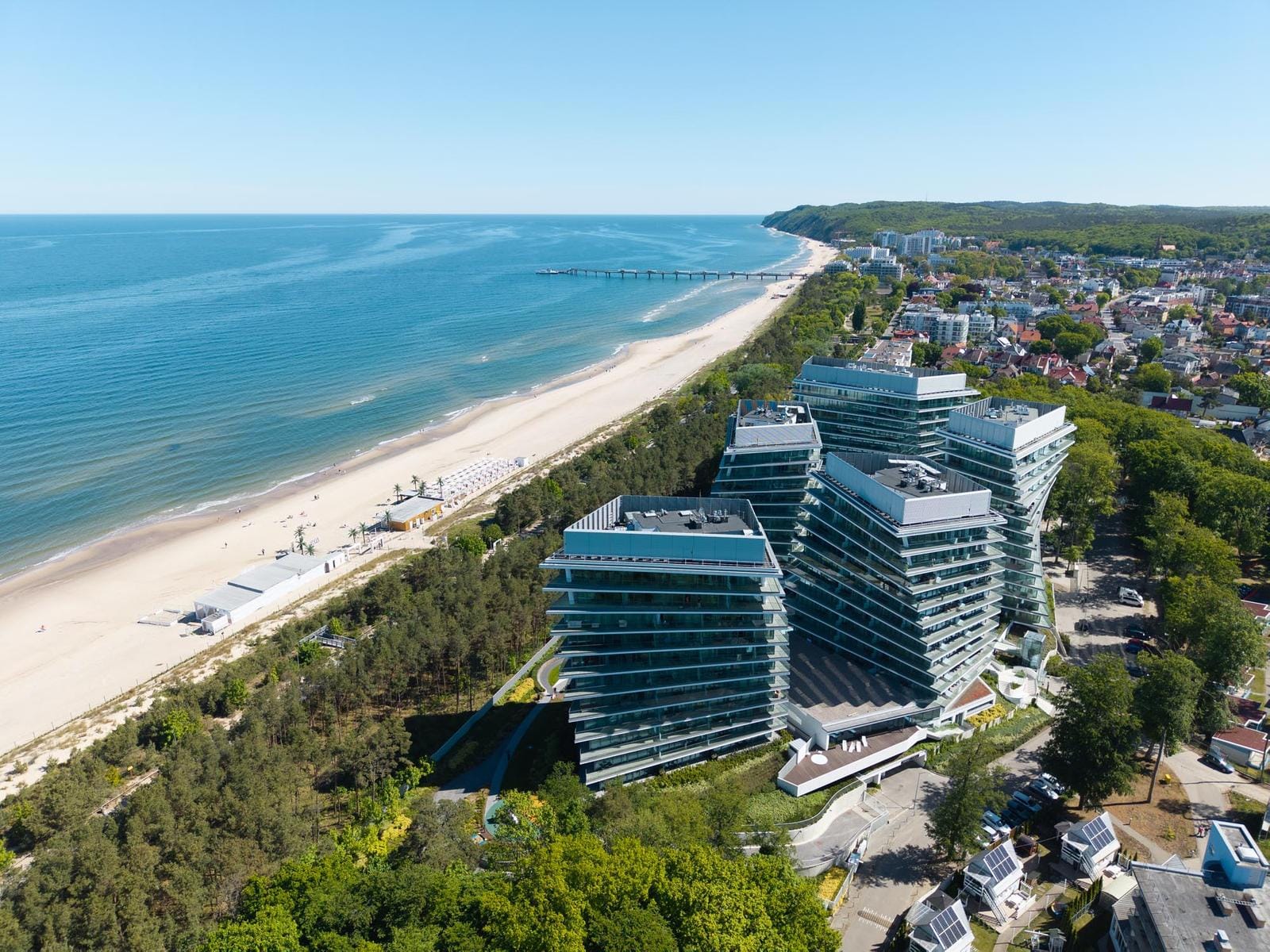 Moderner Hotelkomplex an der Ostseeküste mit Sandstrand und bewaldeter Umgebung.