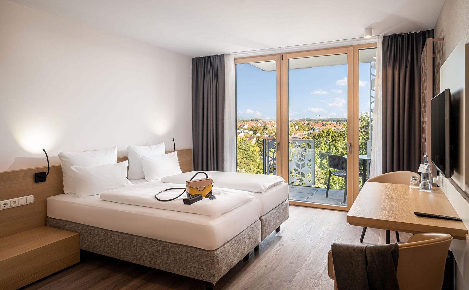 Hotelzimmer mit Doppelbett, modernem Design, Balkon mit Stadtblick und hellem Holzdekor.