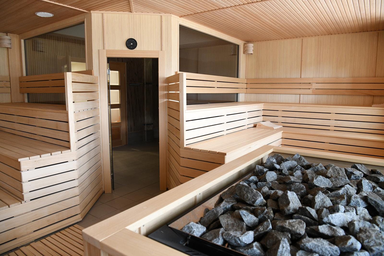 Holzsauna mit Liegebänken, offener Tür und Steinelementen, warmes Ambiente.