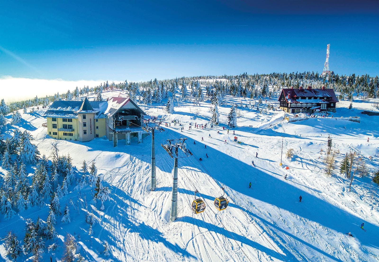 Schneebedeckte Skipiste mit Skifahrern, Seilbahn, und Gebäuden im Winter.