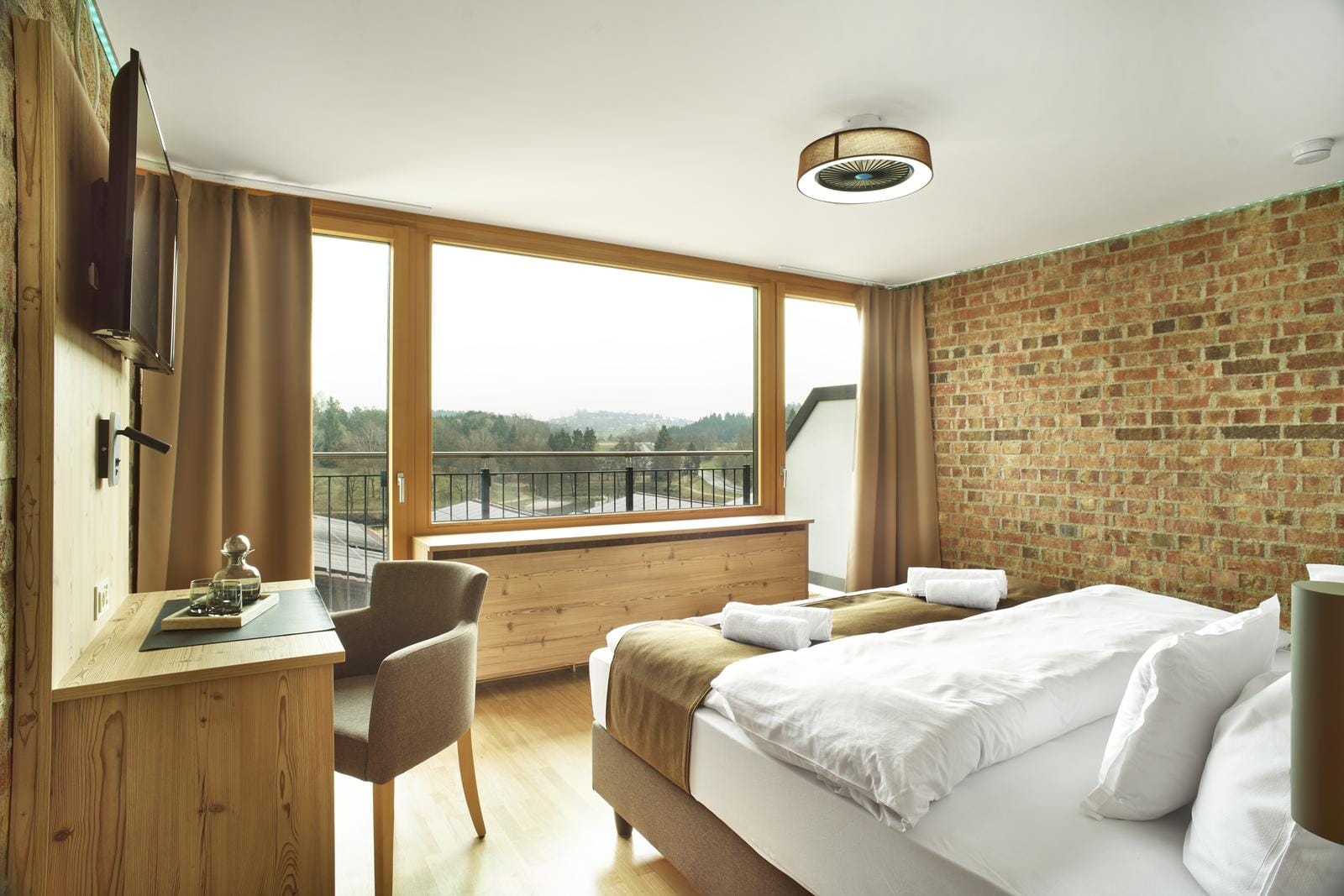 Hotelzimmer im rustikalen Stil mit Backsteinwand, hellem Holz und großer Fensterfront.