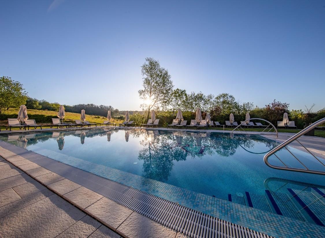 Klares Pool im Freien, umgeben von Liegen und Sonnenschirmen, bei Sonnenuntergang.