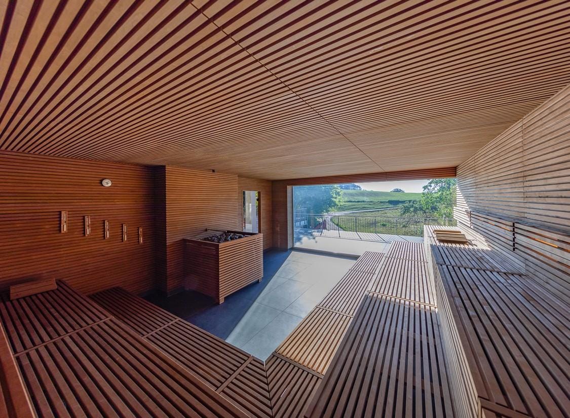Moderne Sauna mit Holzverkleidung, großem Fenster und Blick auf grüne Landschaft.