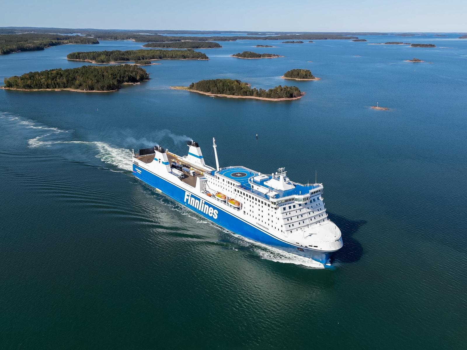 Weiße und blaue Fähre auf blauem Meer, umgeben von grünen Inseln.