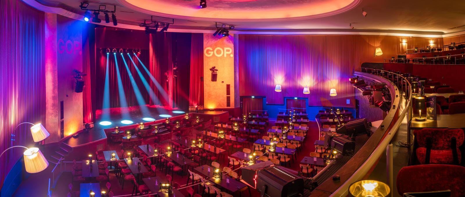 Varieté-Theater mit Bühne, stimmungsvolle Beleuchtung, rote Vorhänge, elegante Sitzreihen.