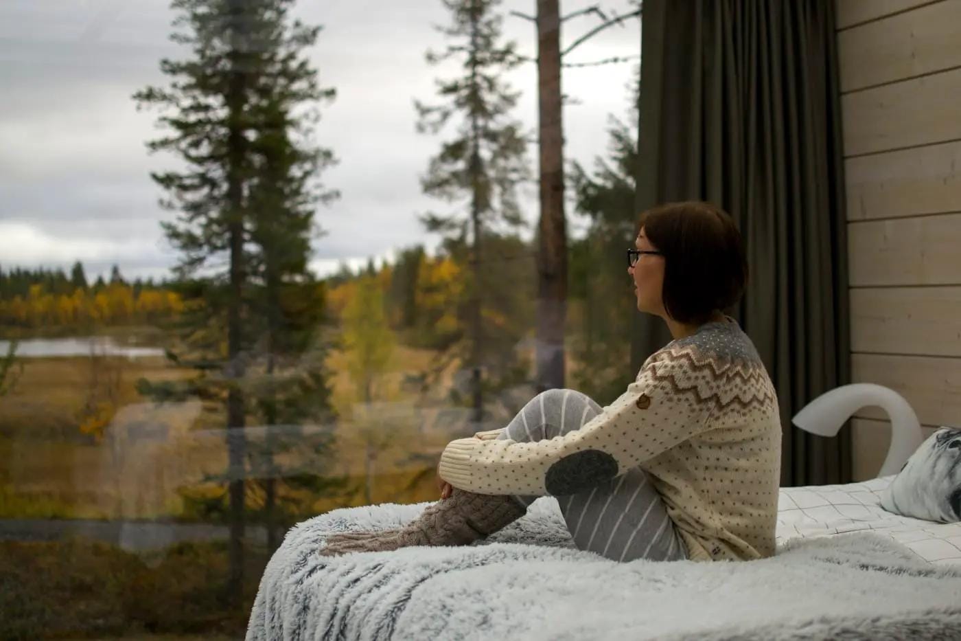Gemütliches Zimmer mit Panoramafenster, Blick auf herbstlichen Wald, ruhige Atmosphäre.
