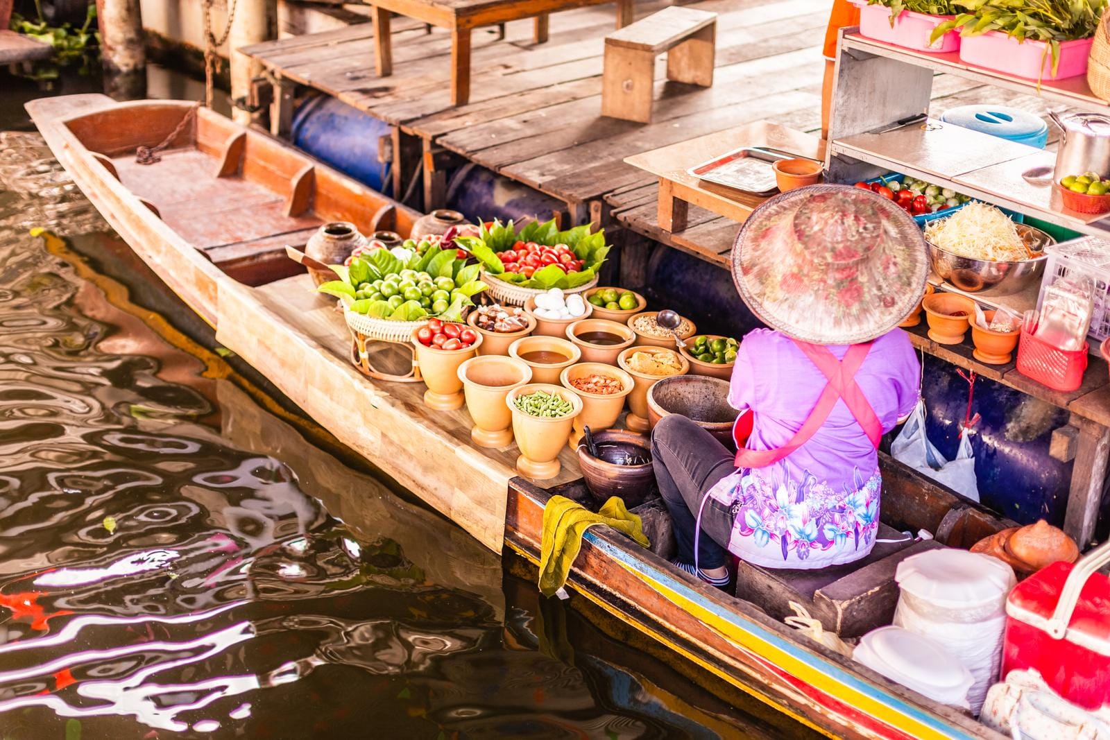 Frau verkauft frisches Gemüse auf einem bunten Boot auf einem schwimmenden Markt.