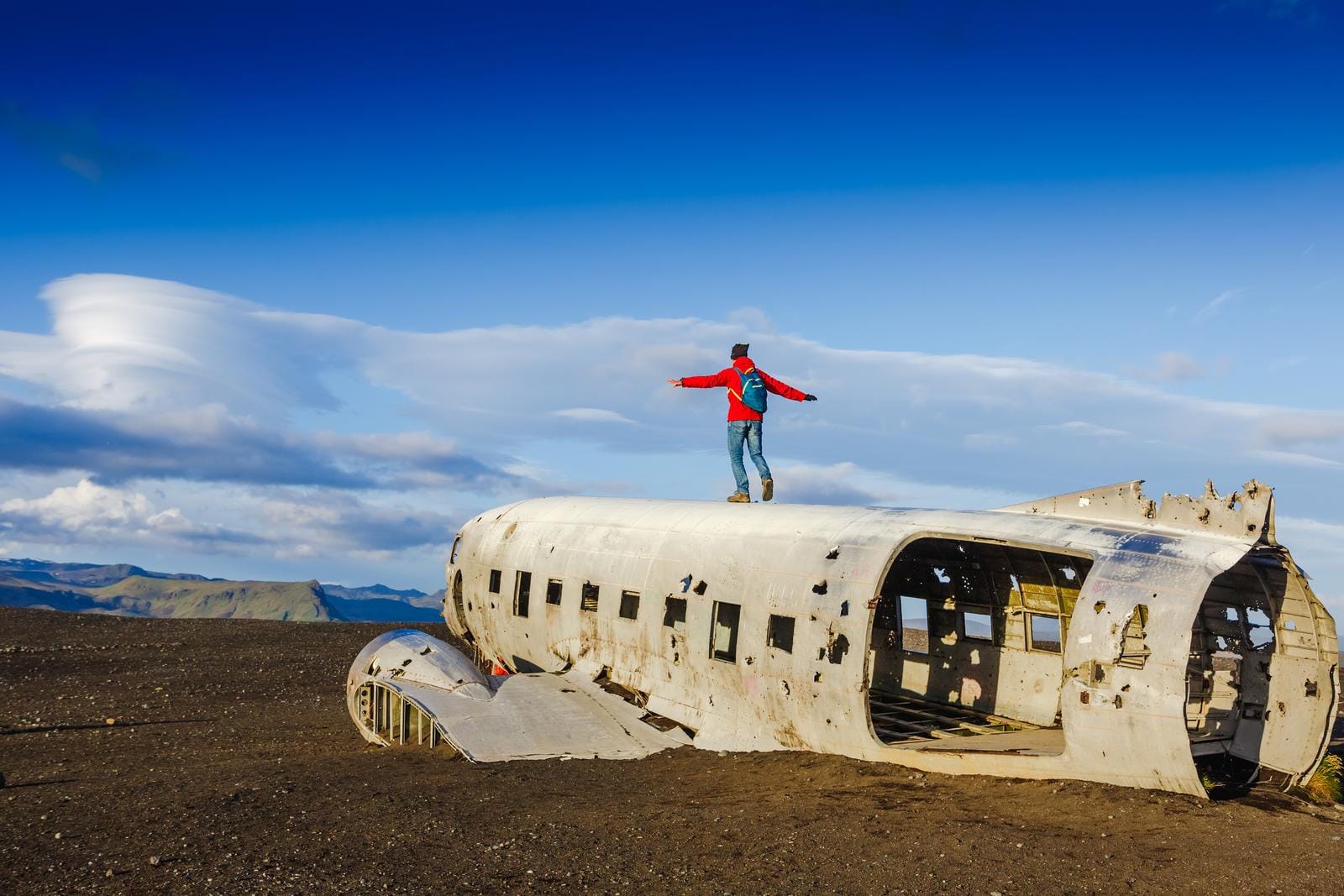 Verlassener Flugzeugwrack auf schwarzem Sand in Island, blauer Himmel, Person darauf.