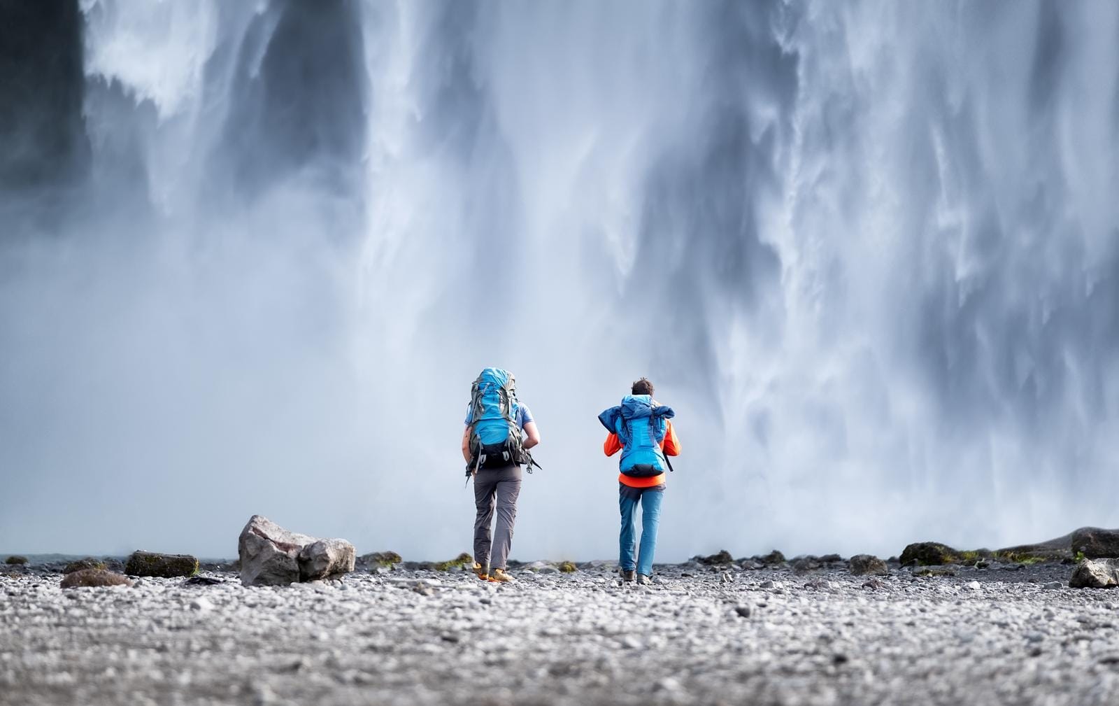 Zwei Wanderer vor einem rauschenden Wasserfall in Island.
