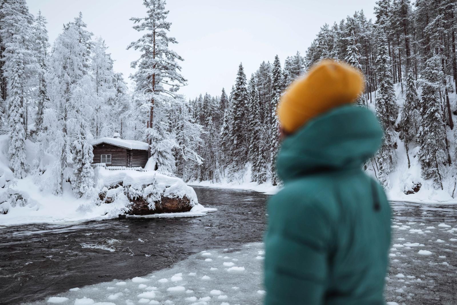 Schneebedeckte Landschaft mit Fluss und Hütte im Wald, winterlich und ruhig, Finnland.