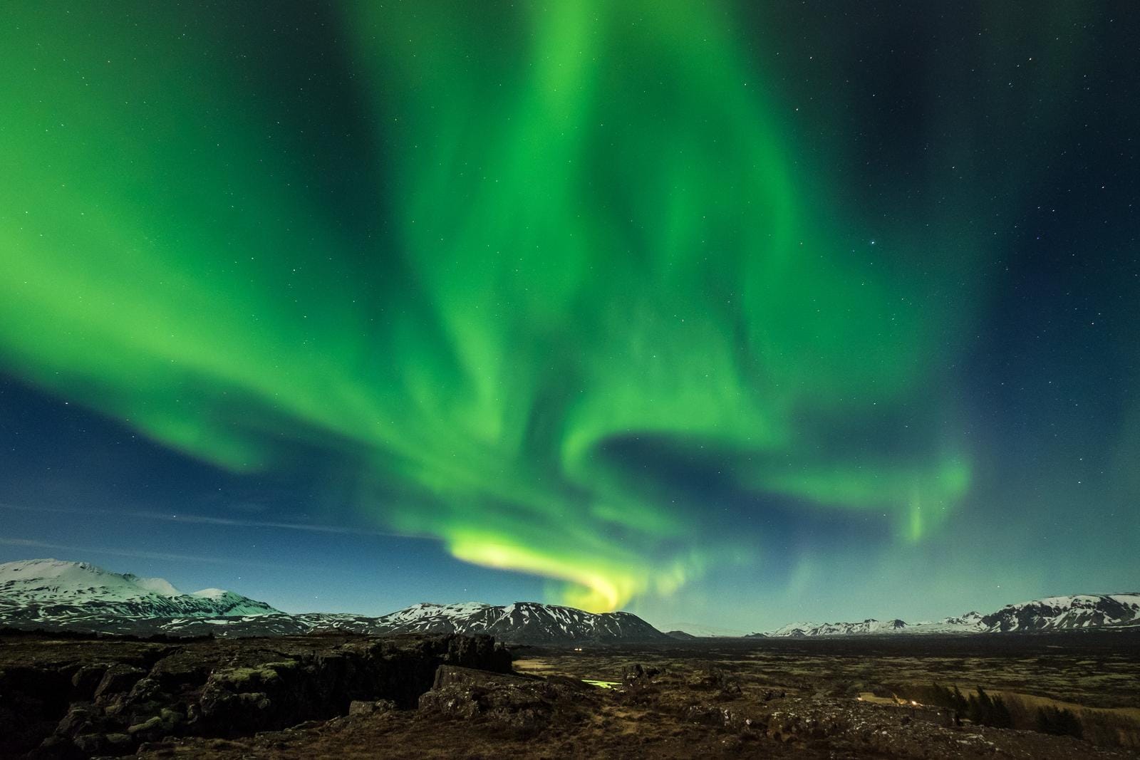 Nordlichter über schneebedeckten Bergen in Island bei klarem Nachthimmel.