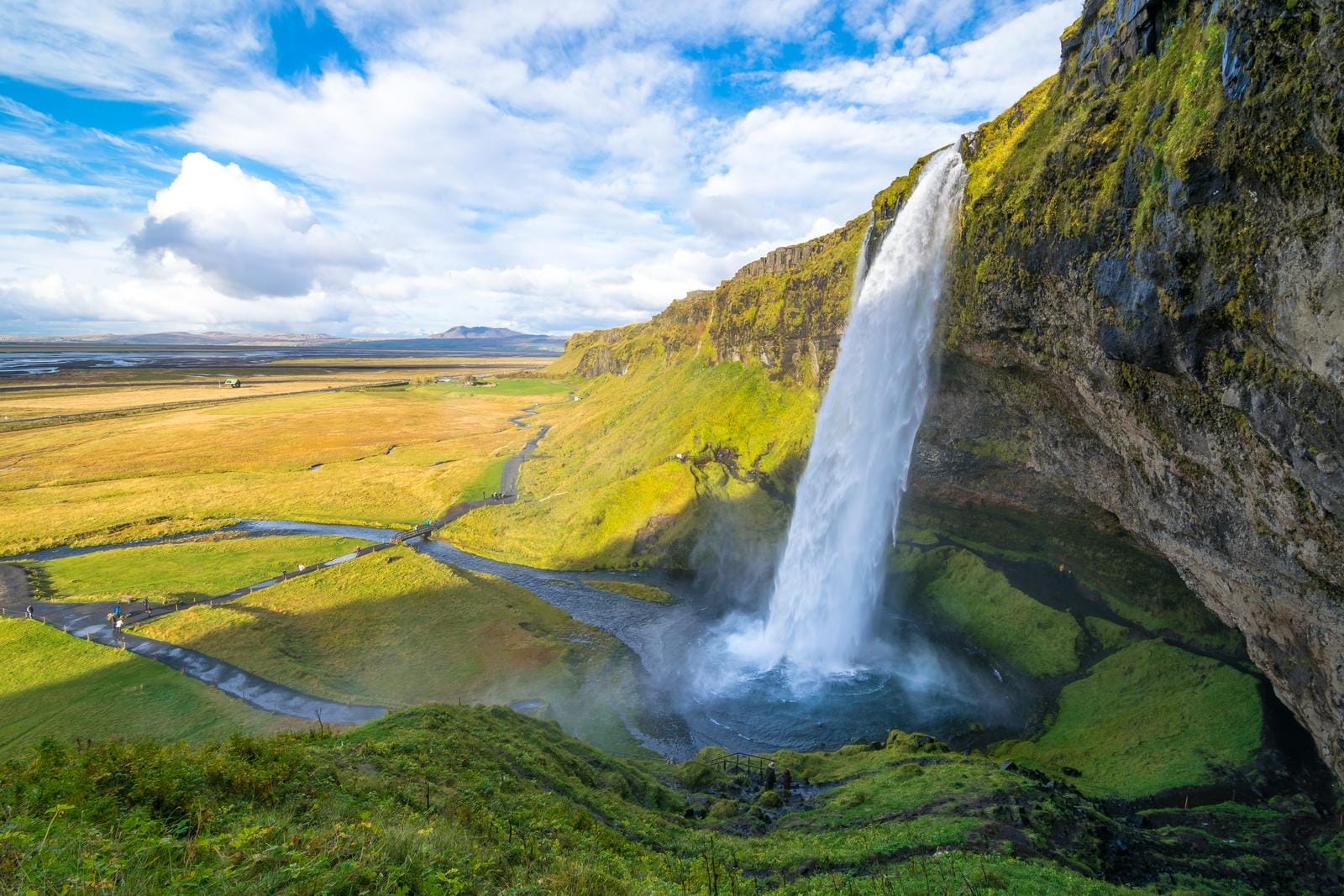 Wasserfall Seljalandsfoss, Island, in grüner Landschaft unter blauem Himmel.