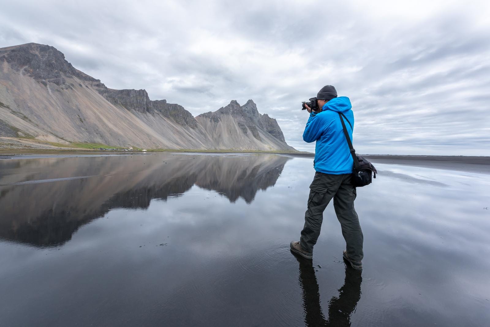 Fotograf am reflektierenden Strand von Stokksnes, Island, vor dramatischen Bergen.
