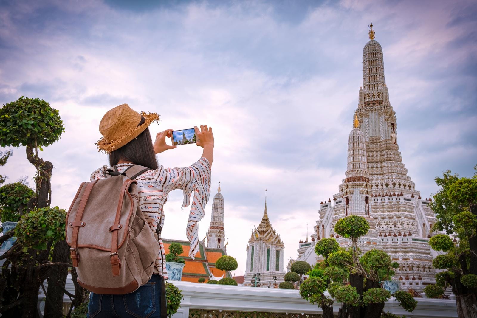 Frau fotografiert Wat Arun in Bangkok, Thailand, bei bewölktem Himmel.