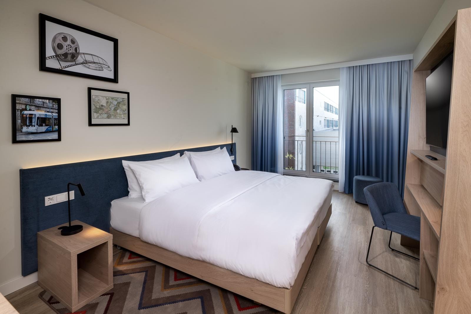 Modernes Hotelzimmer mit Doppelbett, Holzdetails, Kunst an der Wand und blauem Dekor.