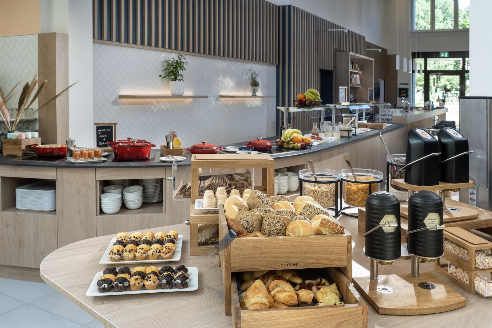 Modernes Hotelbuffet mit frischem Gebäck, Früchten und Cerealien in heller Atmosphäre.