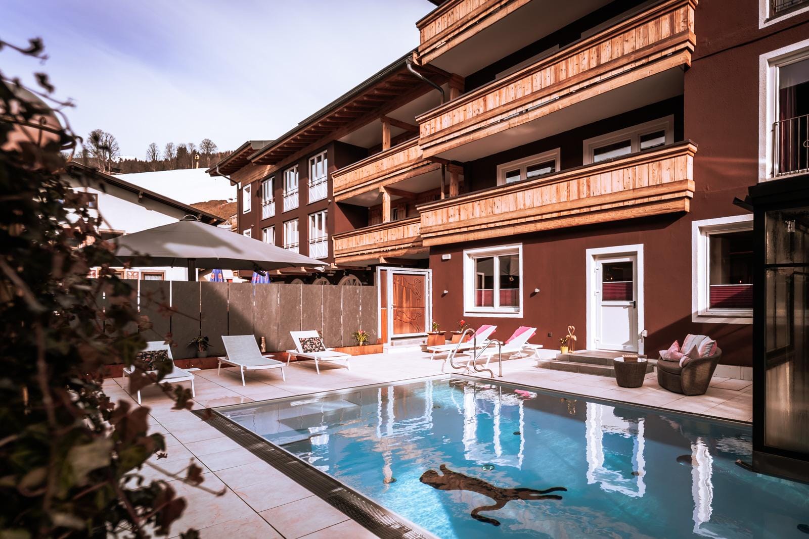 Außenpool mit Liegen, Holzbalkonen und brauner Fassade in alpinem Hotelstil.