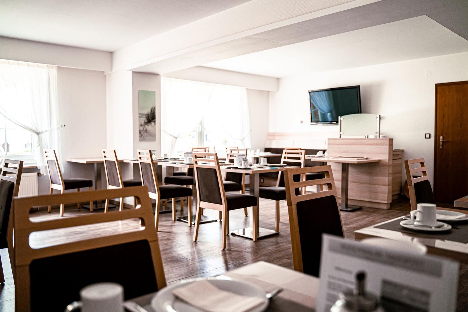 Helles Hotelrestaurant mit Holzstühlen, gedeckten Tischen und Fensterlicht.