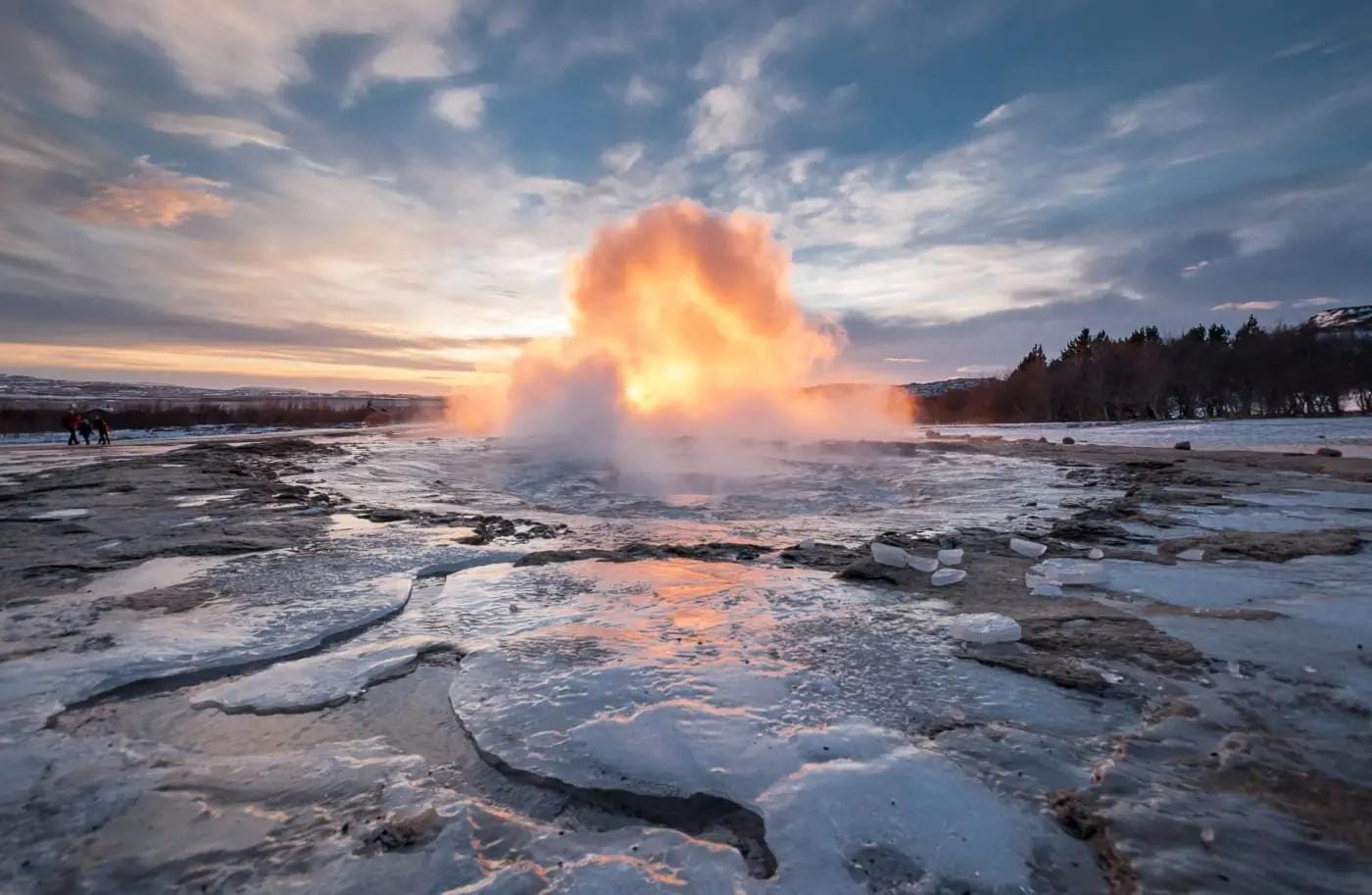 Geysir in Island bei Sonnenuntergang, dampfend mit buntem Himmel.