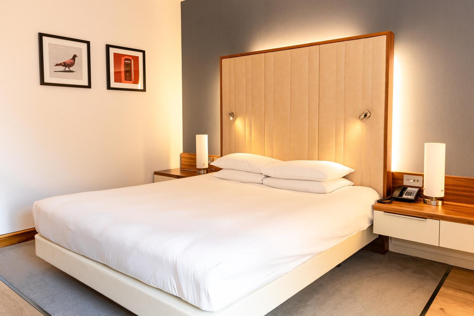 Modernes Hotelzimmer mit großem Bett, hellem Holz, stilvollen Lampen und Wandkunst.