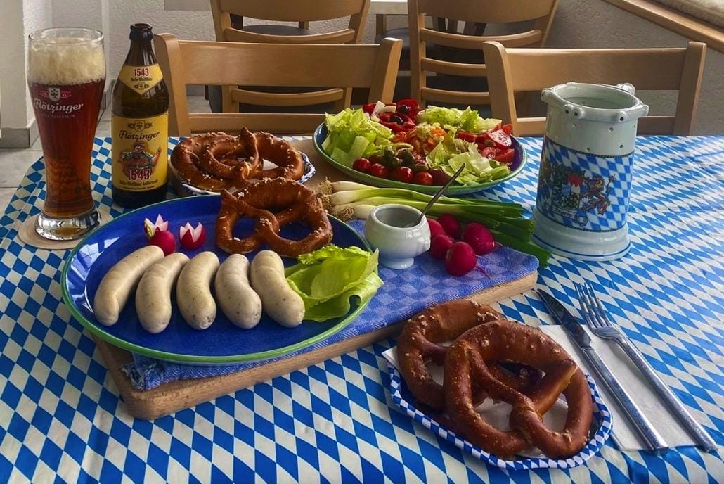 Bayerischer Genuss in München: Weißwürste, Brezn und Bier auf typisch blau-weißem Tischtuch.