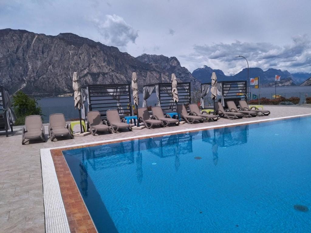Hotelpool mit Liegestühlen, Berg- und Seepanorama im Hintergrund.