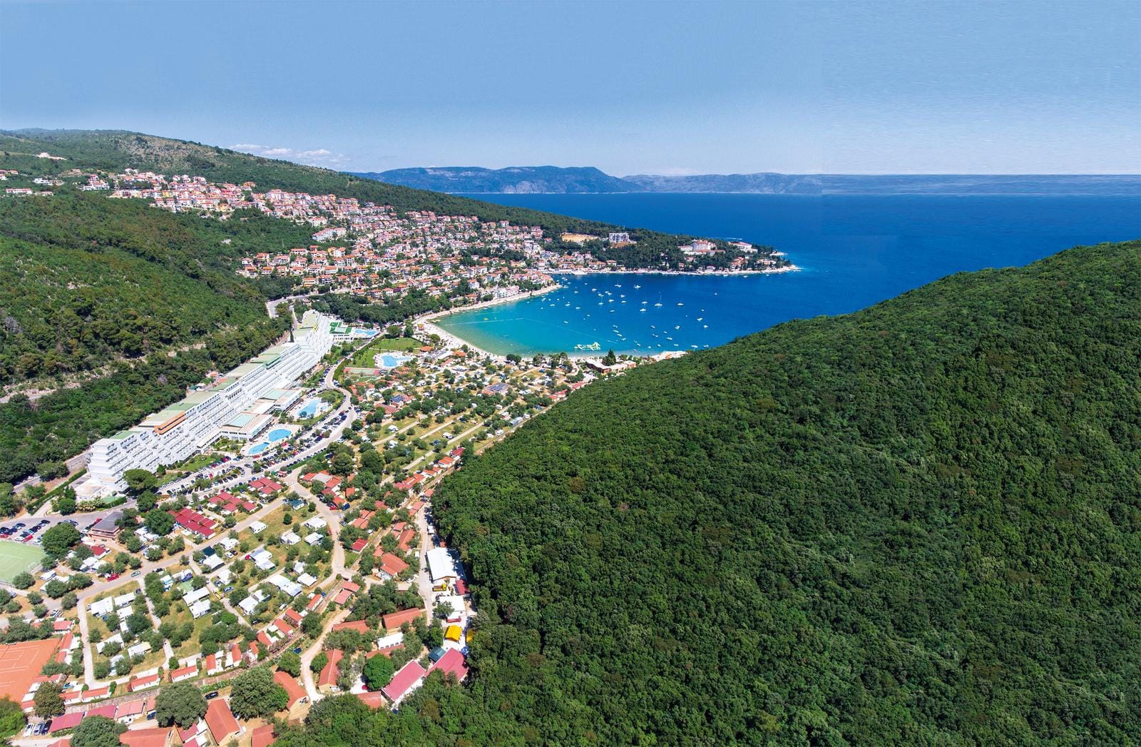Luftaufnahme von Rabac, Kroatien: grüne Hügel, Strand mit klarem Wasser und Boote.