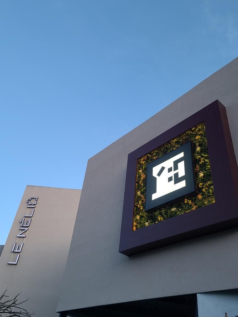 Modernes Gebäude mit schlichtem Logo auf grau-beiger Fassade unter klarem, blauem Himmel.