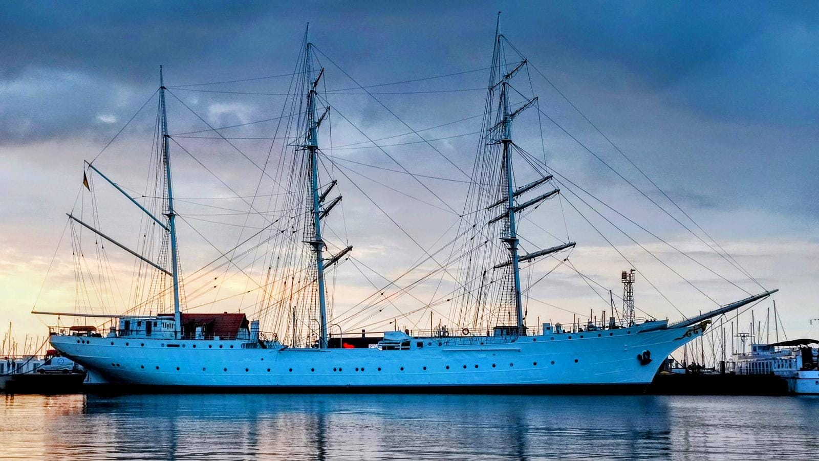 Großes Segelschiff im Hafen bei Sonnenuntergang, blauer Himmel und Wasser.