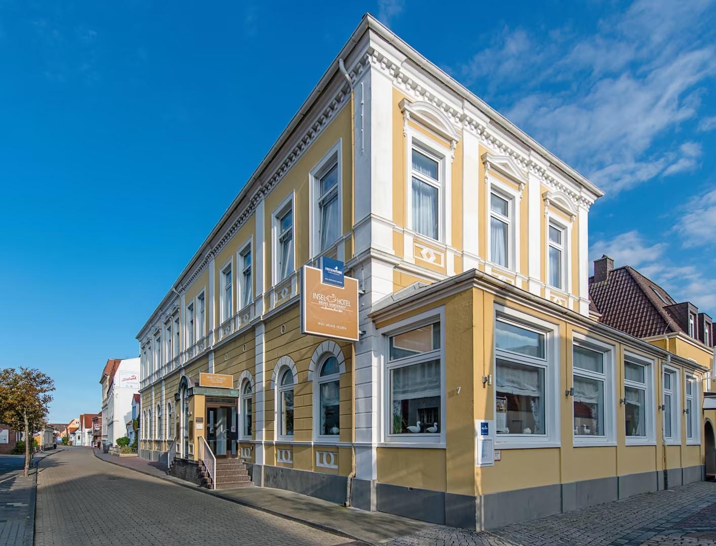 Gelbes Hotel im klassischen Stil mit weißer Fassade und Bogenfenstern bei blauem Himmel.