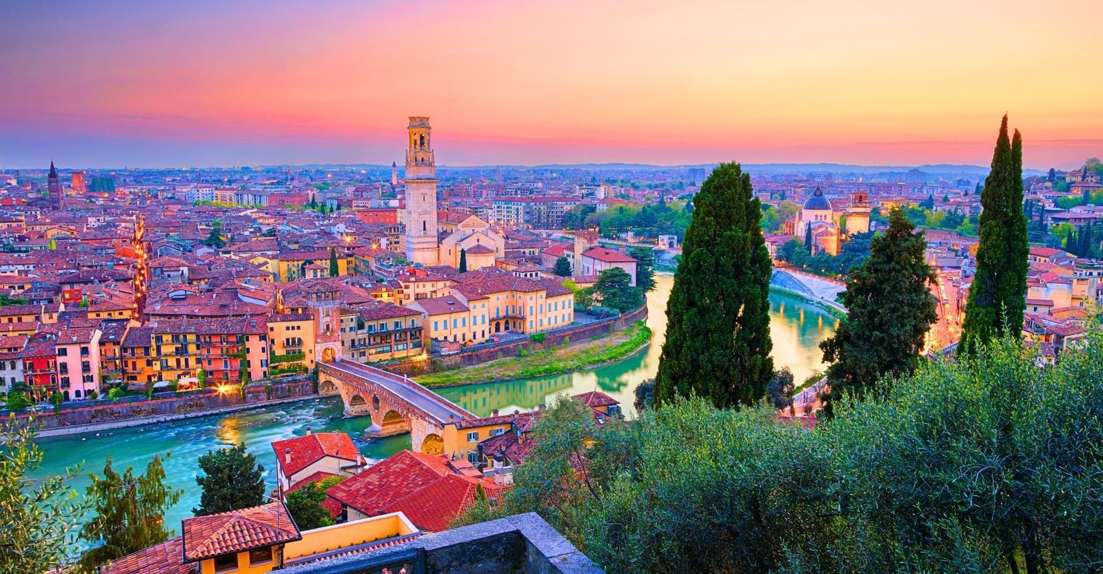 Blick auf Verona, Italien bei Sonnenuntergang, mit Adige-Fluss und historischen Gebäuden.