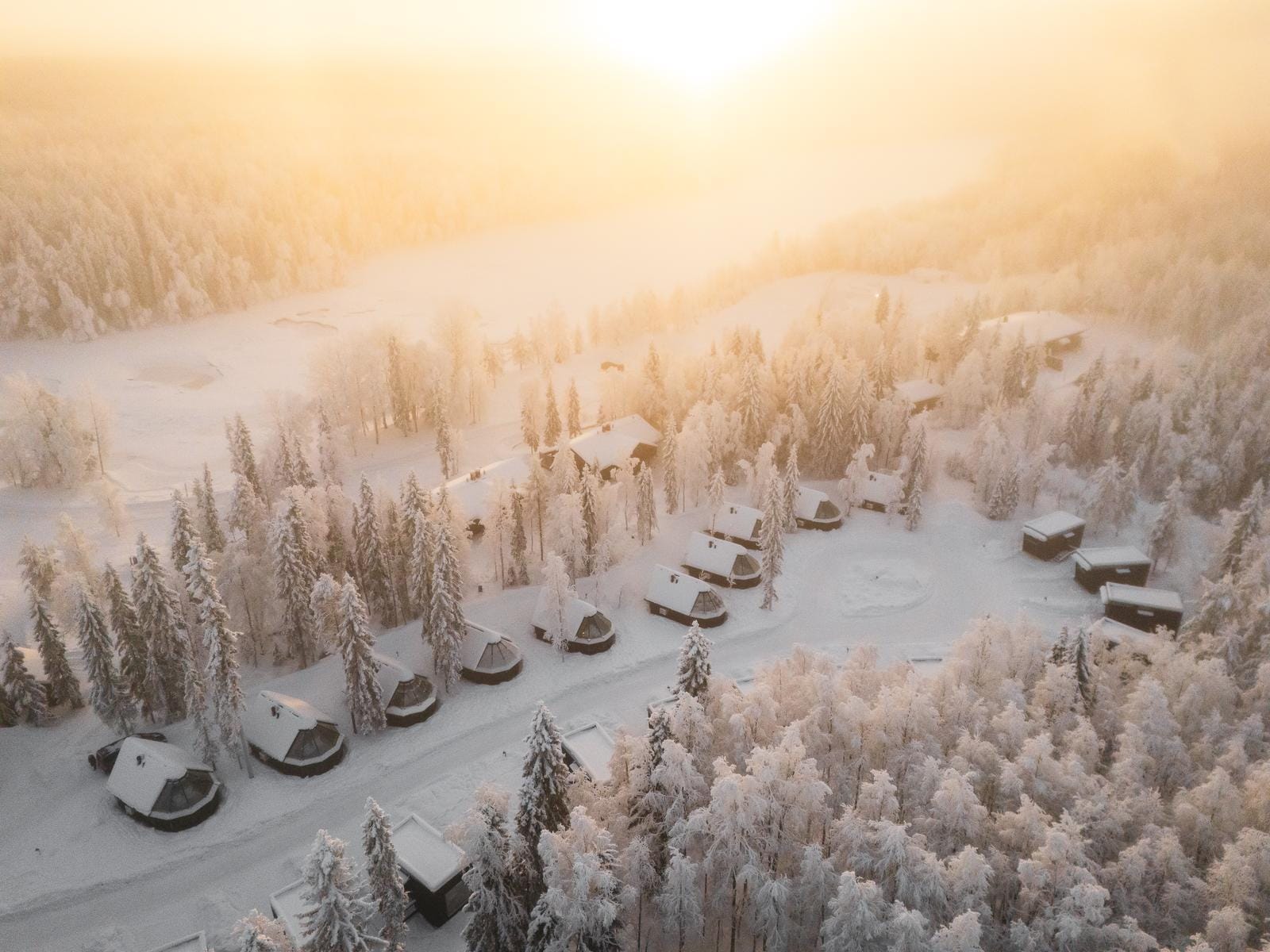 Schneebedecktes Waldresort bei Sonnenaufgang, gemütliche Kabinen und vereiste Bäume.