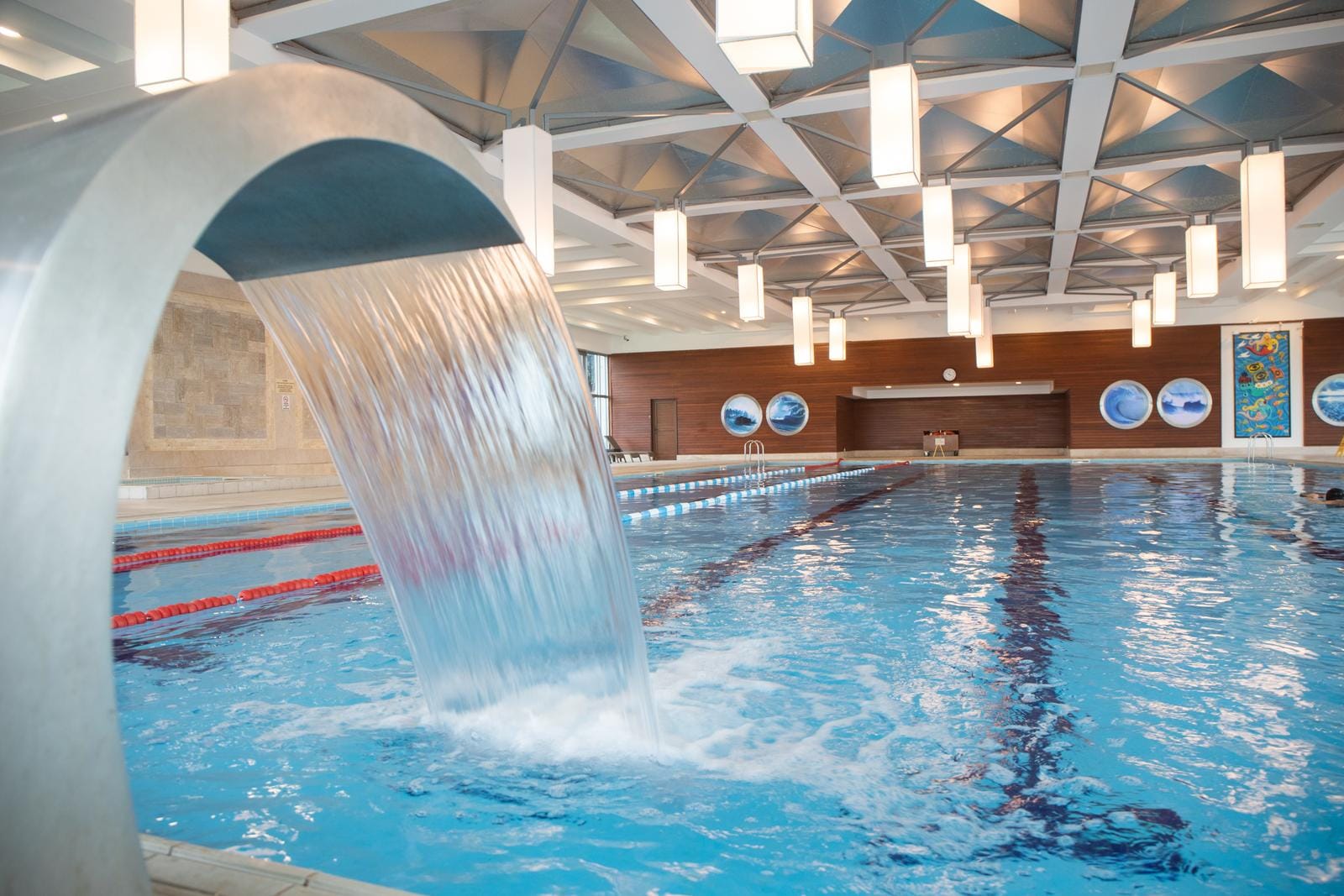Moderner Indoor-Pool mit Wasserfall, blauer Decke und hölzerner Wandverkleidung.