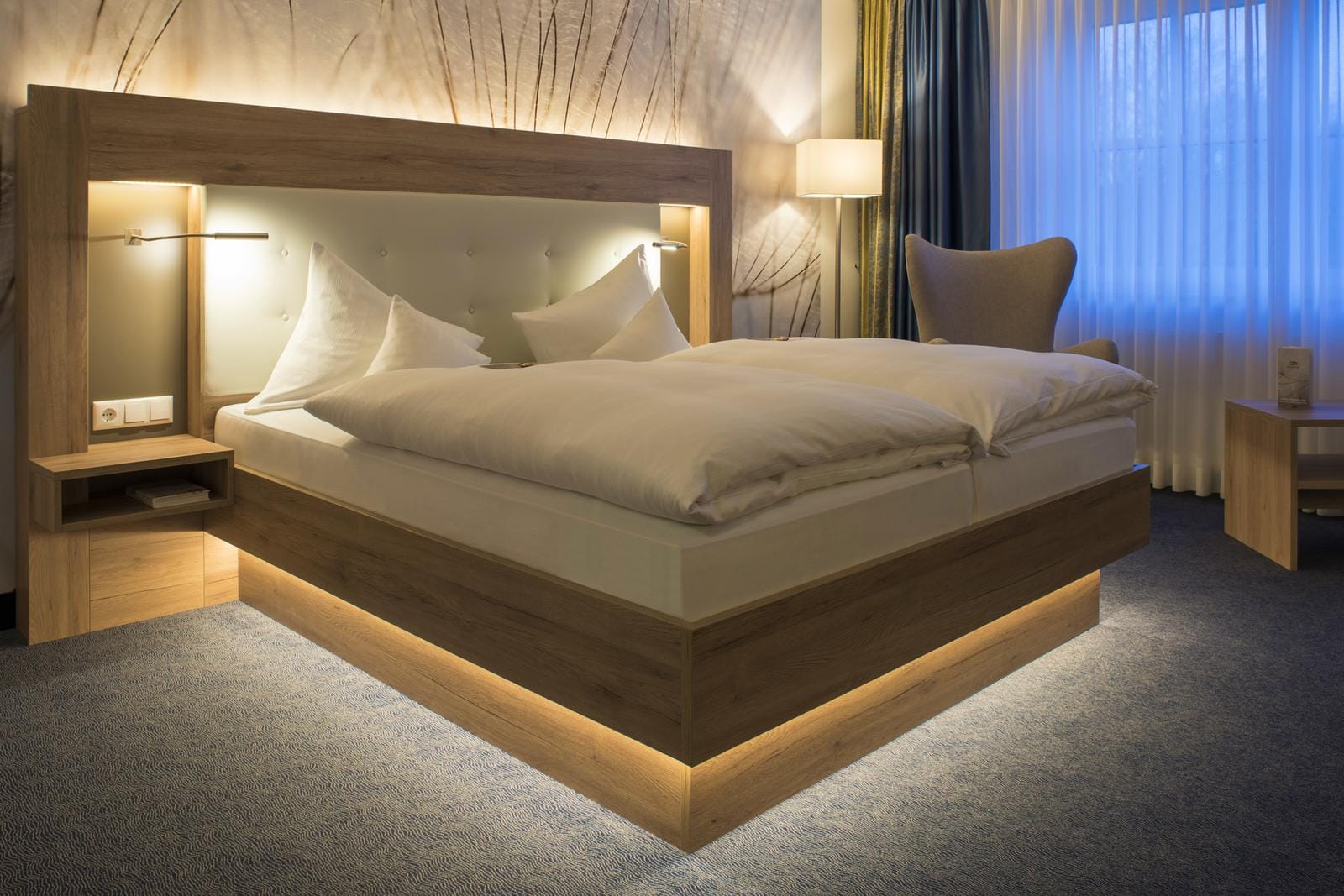 Modernes Hotelzimmer mit Holzmöbeln, Beleuchtung im Bettgestell und sanften Erdtönen.