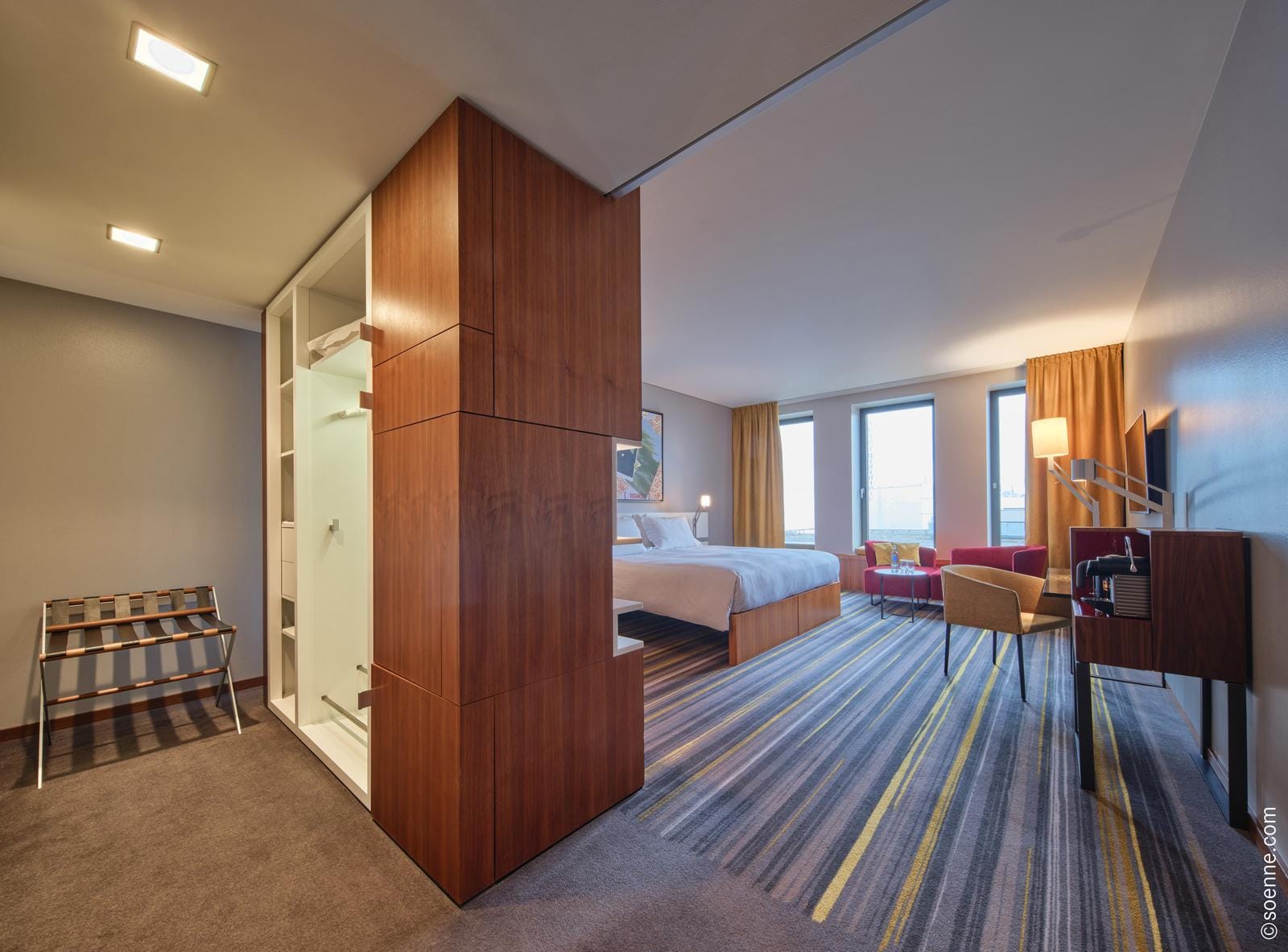 Modernes Hotelzimmer mit Doppelbett, bunten Streifen-Teppich und großen Fenstern.