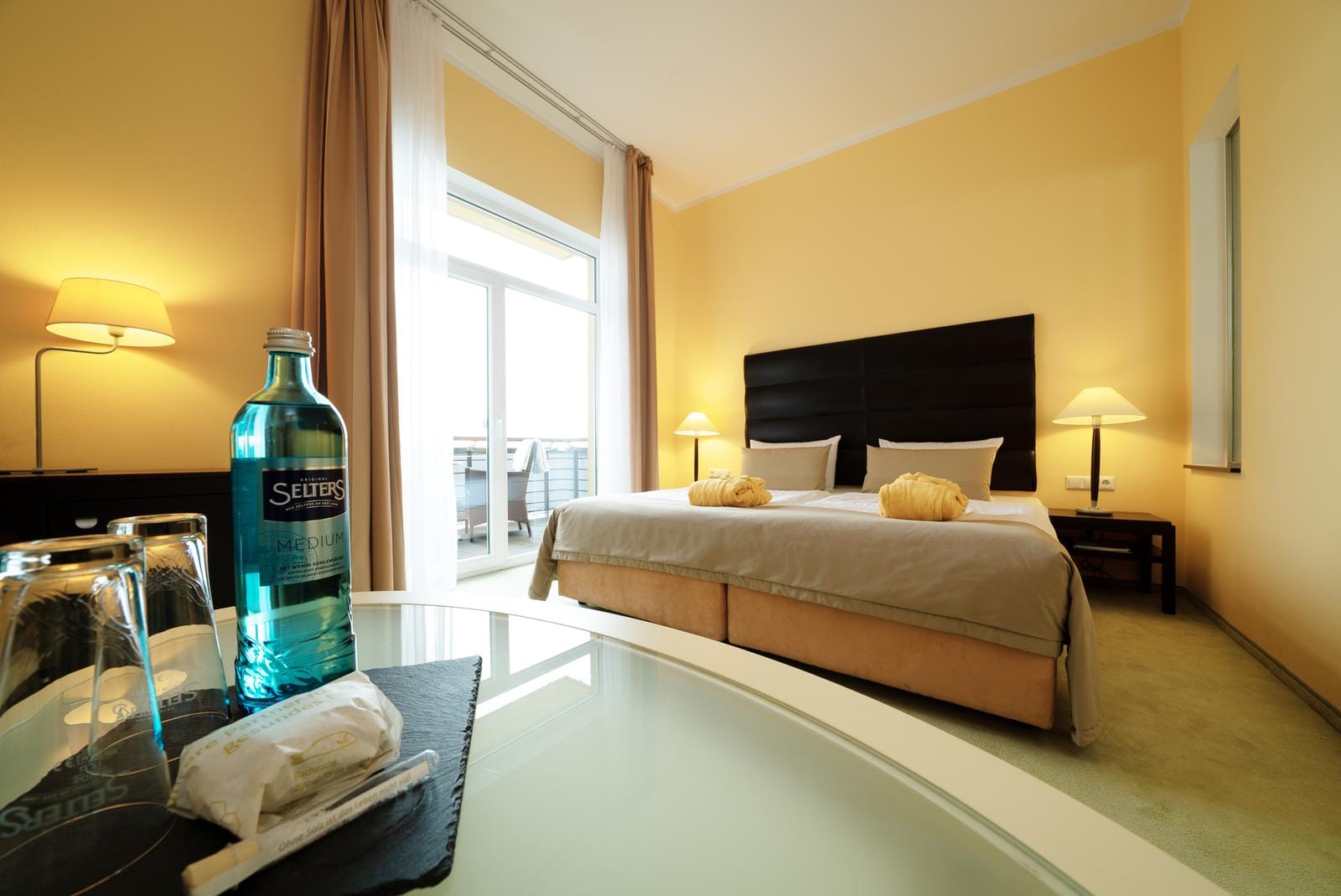 Helles Hotelzimmer mit Doppelbett, hellgelben Wänden und Balkonzugang, modern und einladend.