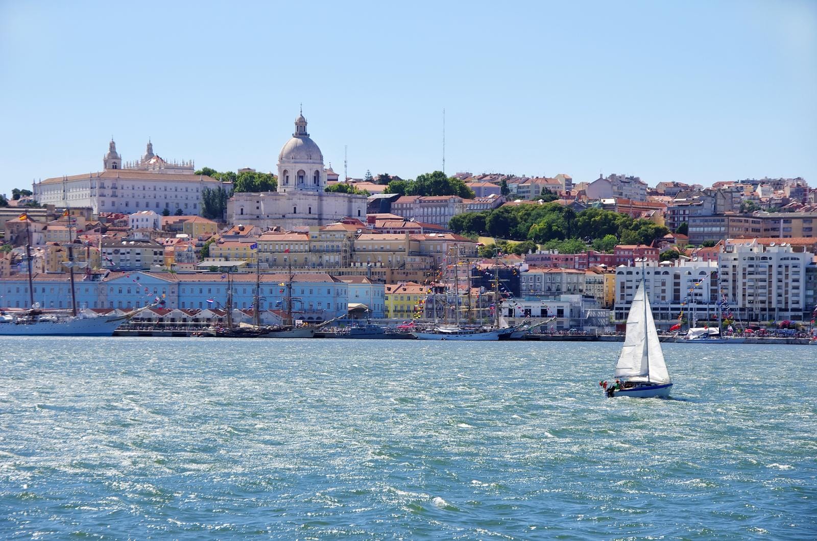 Segelboot vor farbenfroher Altstadt von Lissabon, Portugal; sonniger Himmel.