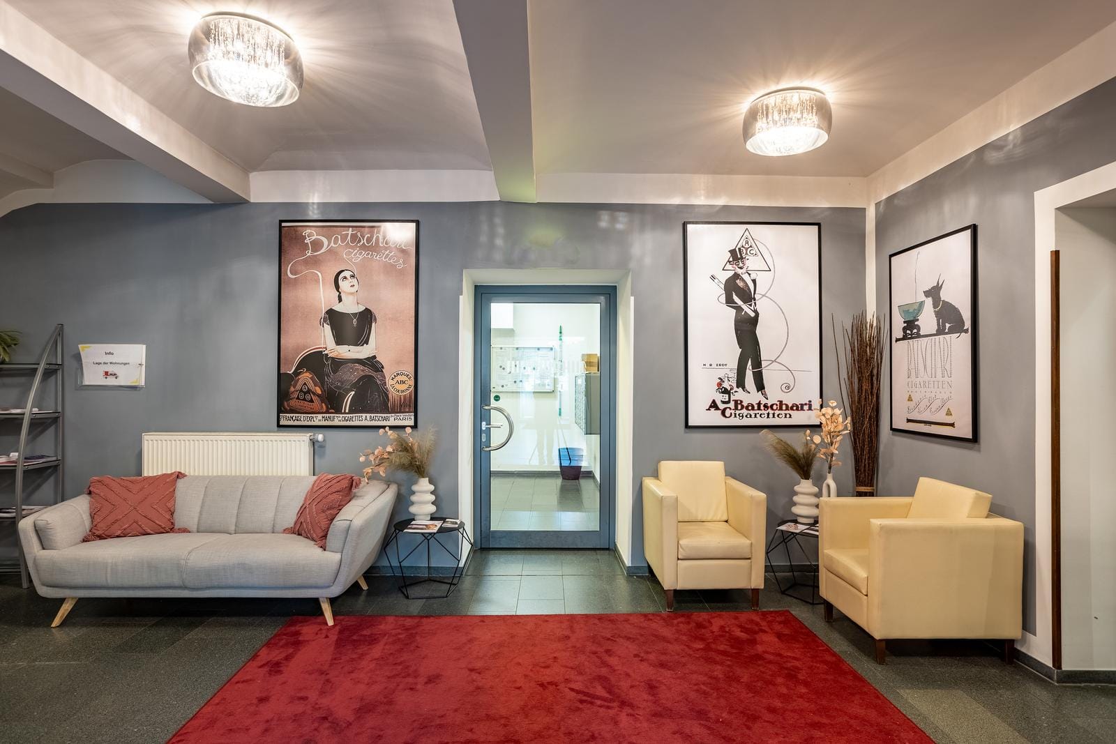 Moderne Hotellobby mit grauer Wand, Retro-Postern, Sofa, Sesseln und rotem Teppich.