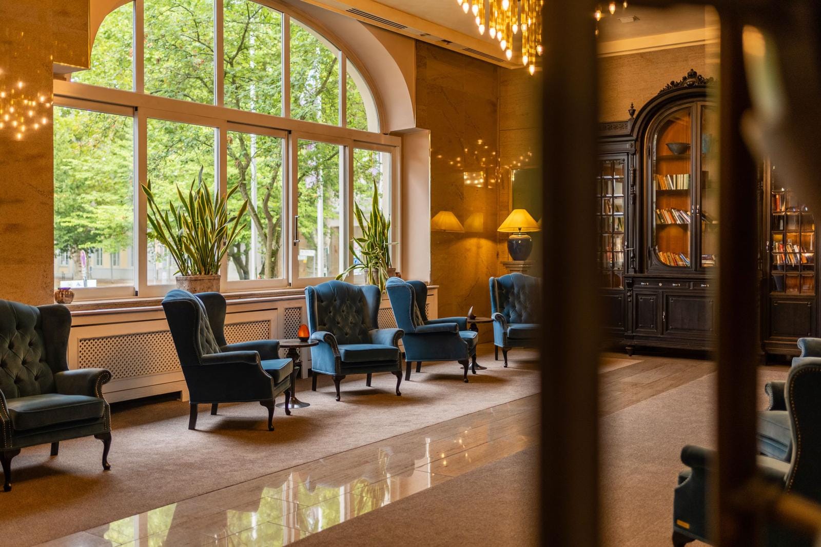 Elegante Hotel-Lobby mit blauen Sesseln, großer Fensterfront und Bücherregal.