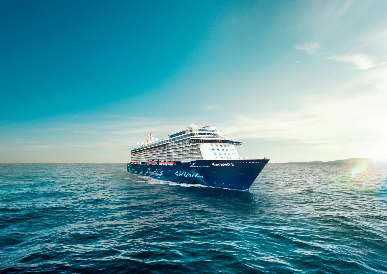 Mein Schiff 5 auf offenem Meer, blauer Himmel, sanfte Wellen, Sonnenlicht.
