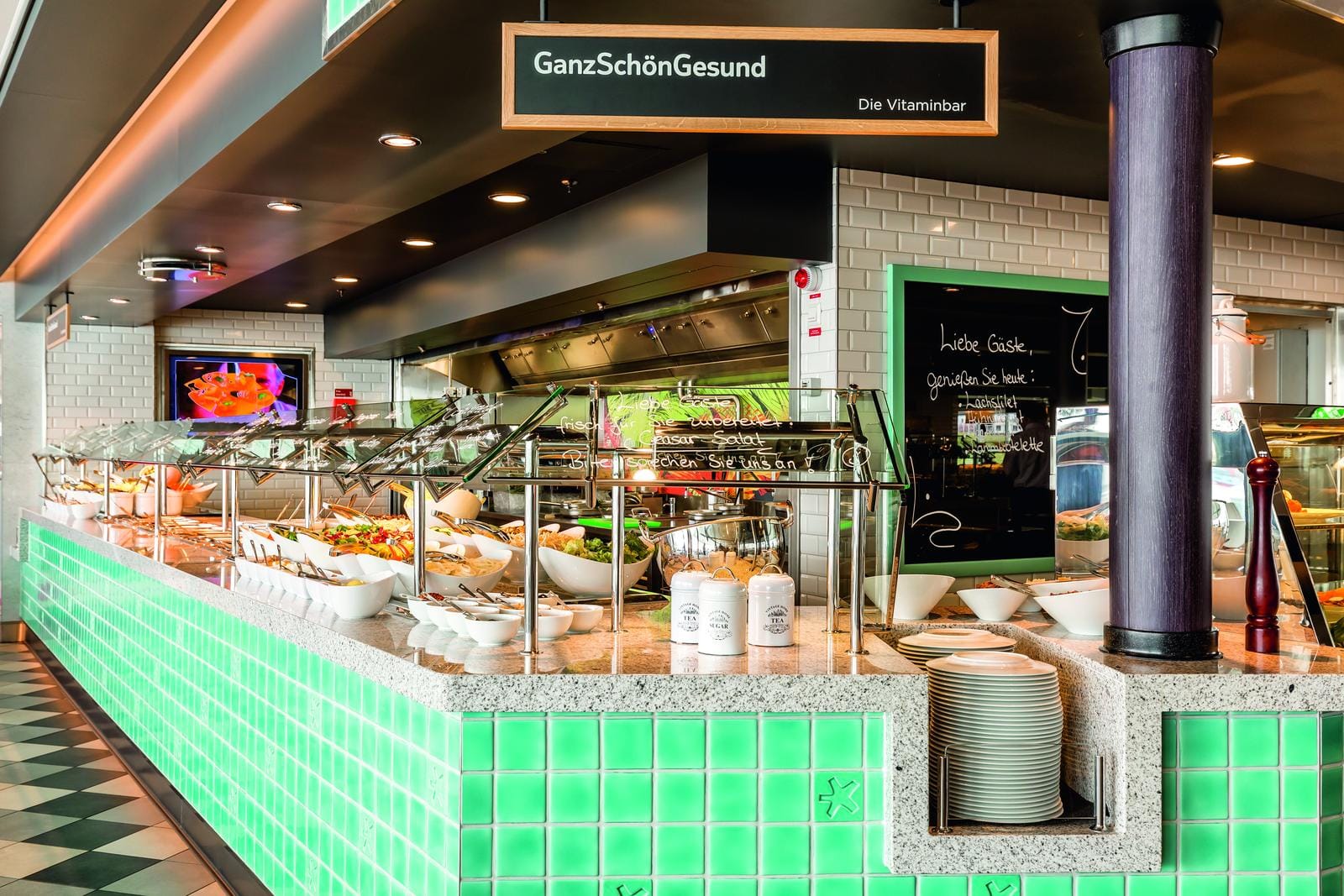 Helles Hotelrestaurant mit Vitaminbar, grünen Kacheln und bunt angerichtetem Buffet.