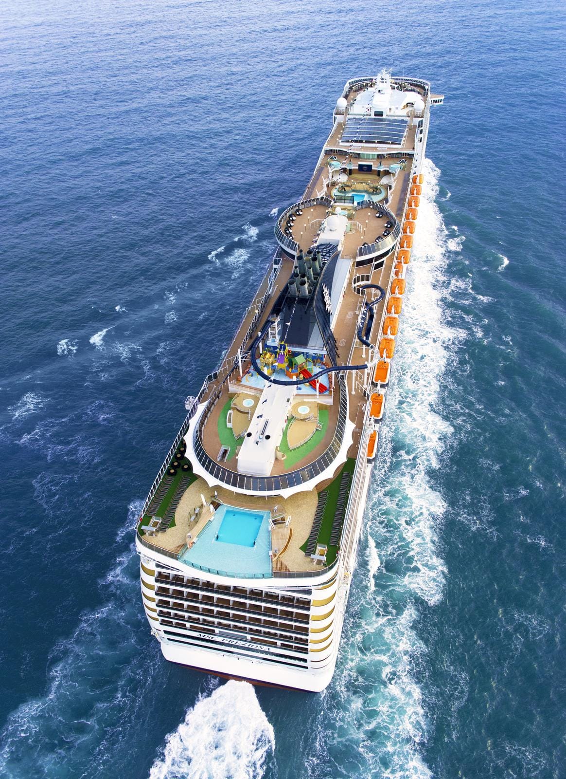 Großes Kreuzfahrtschiff mit Pools und bunter Wasserrutsche auf dem offenen Meer.